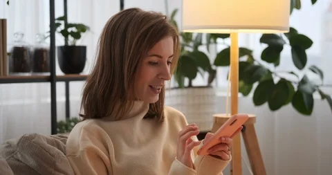 Woman laughing while using mobile phone at home Stock Footage 125068555