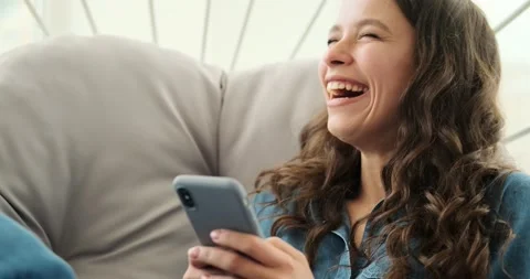 Woman laughing while using mobile phone sitting on luxury chair Video stock 156519886