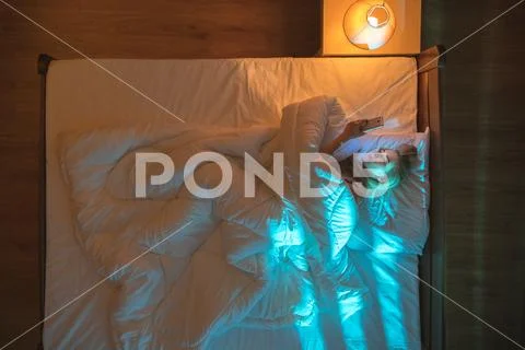 The woman lay on the bed and phone. Evening night time. View from above Stock Photos