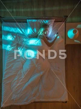 The woman lay on the bed and phone. Evening night time. View from above Stock Photos