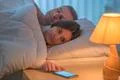The woman lay on the bed with man and phone. Evening night time Photo