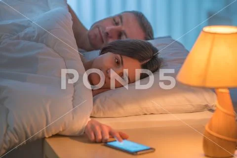 The woman lay on the bed with man and phone. Evening night time Stock Photos