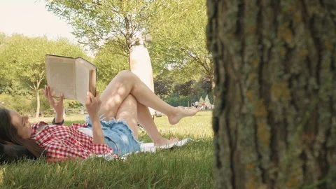 Woman lay down or relaxing on green grass reading book in summer or spring Stock Footage