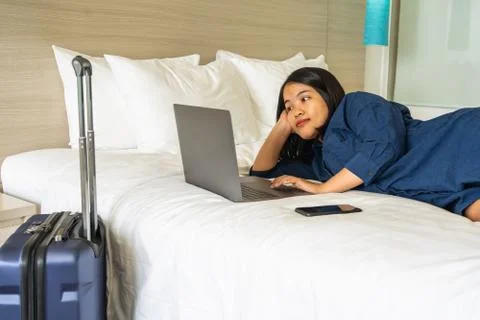 Woman laying on bed while using laptop next to suitcase Stock Photos
