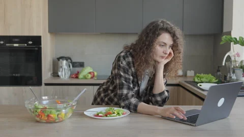Woman Leaning On Hand While Browsing Laptop During Lunch In Modern Kitchen Stock Footage 308254697