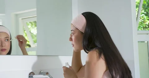 Woman leaning at vanity checking mirror before using dropper applying skincare Stock Footage 341241900