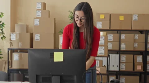Woman leans over computer checking orders and sorting packages in a packing.. Stock Footage 337369390