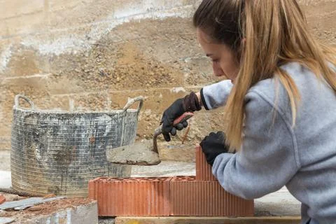 Woman learning for the first time to make a brick wall to make her diy house Stock Photos