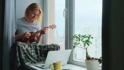 Woman learning to play the ukulele using online musician class on a laptop. Stock Footage 247604417