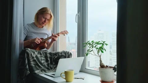 Woman learning to play the ukulele using online musician class on a laptop. Vídeo Stock 249640129