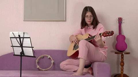 Woman learning to playing classical guitar while sitting on sofa at home Stock Footage 296564721