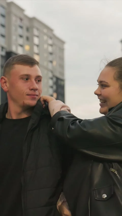 Woman in leather jacket adjusting man puffer jacket and arm position outdoors Stock Footage 345548720