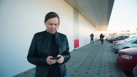 Woman in leather jacket checking phone in supermarket parking lot outside s.. Stock Footage 341662697