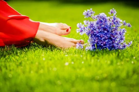 Woman legs on green grass with flower dress. Summer vacation concept. backlit Stock Photos