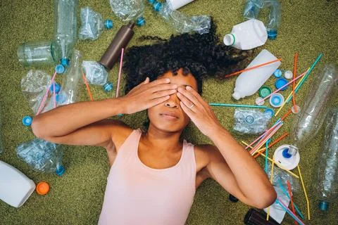 A woman lies on the carpet, surrounded by an array of discarded plastic bottles Stock Photos
