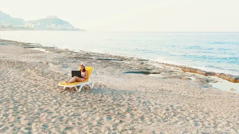 Woman lies on a deck chair, working remotely on a laptop by the sea quadrocopter Stock Footage