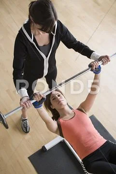 Woman lifting barbell while instructor assisting her Stock Photos