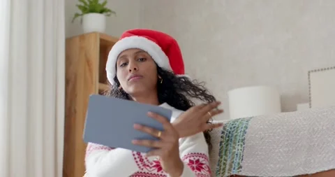 Woman lifting gray tablet to frame selfie, adjusting Santa hat and sweater, Stock Footage 344462020