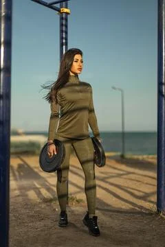 Woman lifting weights on a beachside path during a sunny afternoon in activewear Stock Photos
