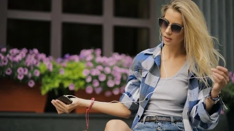 Woman listen music on smart phone sitting in city street Stock Footage