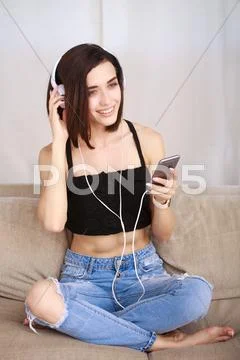 Woman listening music in headphones sitting on sofa in room Stock Photos