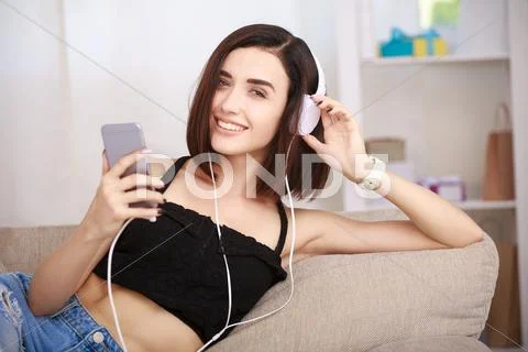 Woman listening music in headphones sitting on sofa in room Stock Photos