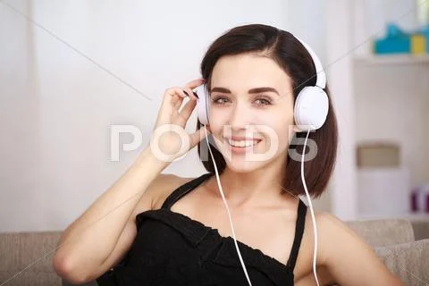 Woman listening music in headphones sitting on sofa in room Stock Photos