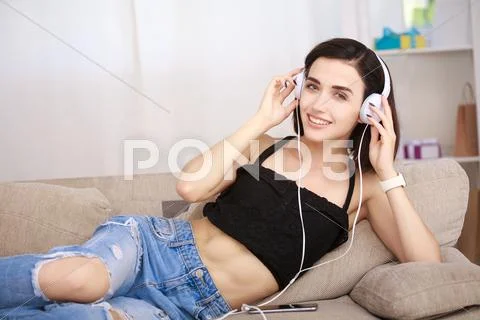 Woman listening music in headphones sitting on sofa in room Stock Photos