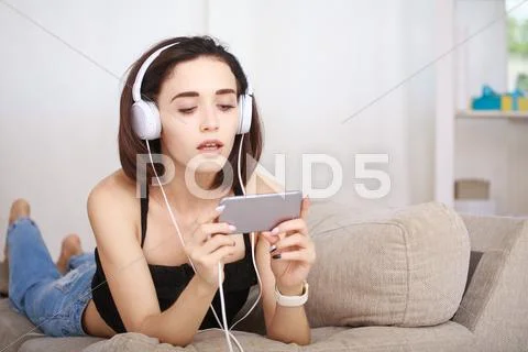 Woman listening music in headphones sitting on sofa in room Stock Photos