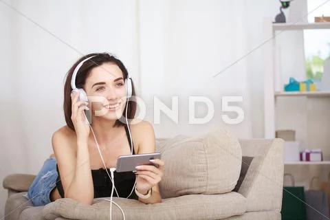 Woman listening music in headphones sitting on sofa in room Stock Photos