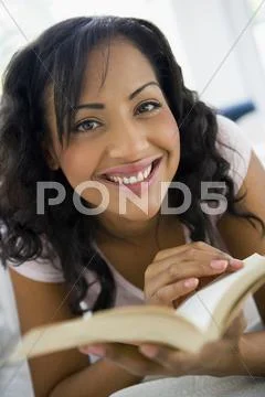 Woman in living room with book smiling (high key/selective focus) Stock-Fotos