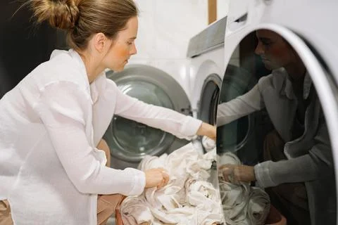 Woman loading white laundry into front-loading washing machine in home laundry Stock-Fotos