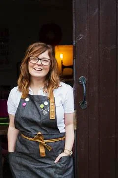 Woman with long brown hair wearing apron and glasses standing in an open Stock Photos