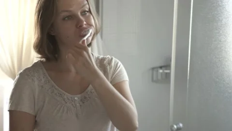 Woman looking at bathroom mirror while brushing teeth Stock Footage 132050326