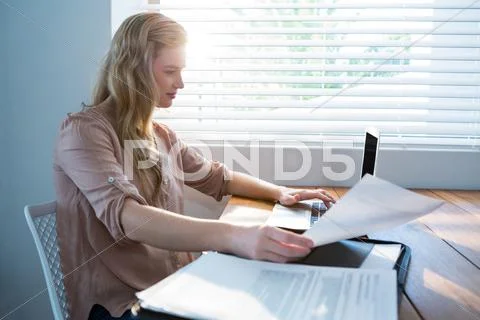 Woman Looking At Bill While Using Laptop
