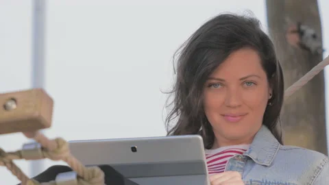 Woman looking at camera lying in hammock on seaside and using laptop. Видео 95941894