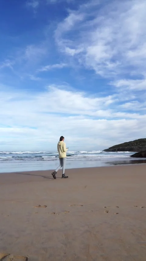 Woman looking at cell phone while walking on the beach Stock Footage 260798587