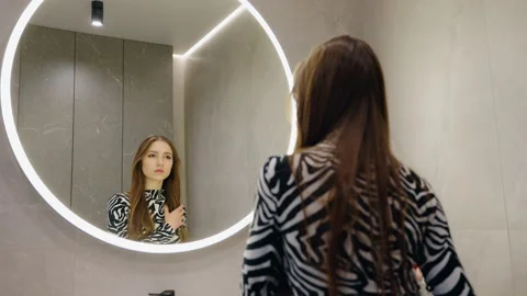 Woman Looking at Her Reflection in an Illuminated Bathroom Mirror Stock Footage 345622806