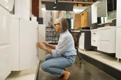 Woman looking inside a cabinet while shopping for furniture in a modern store Stock Photos