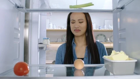 A woman looking inside her empty fridge is frustrated and disappointed. Stock Footage 100098883
