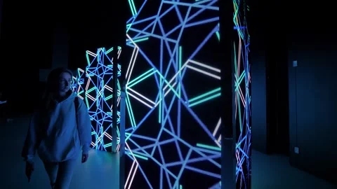 Woman is looking at LED columns with immersive geometric show on screen walls Stock Footage 344313644