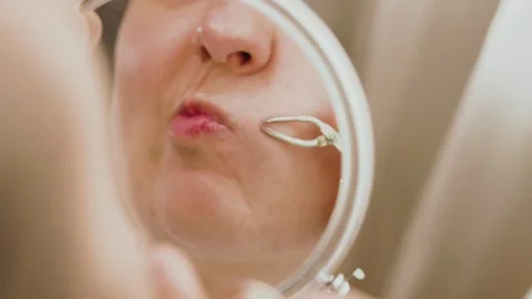 Woman looking in a magnifying mirror, using tweezers for mustache removal.  Stock Footage 335747188