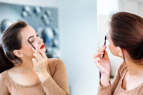 Woman looking in the mirror combing her eyebrows Stock Photos