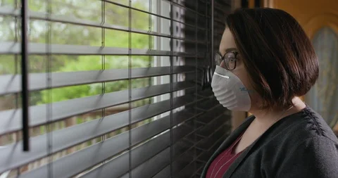 Woman Looking Out Of Window While Wearing White Protective Face Mask PPE 動画素材 129565012