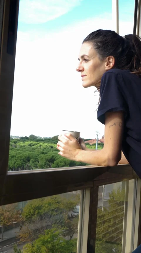 Woman looking out the window while enjoying a coffee Stock Footage 253801388