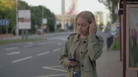 A woman looking at a smartphone screen while waiting for a bus at a bus stop. Stock Footage 155151424