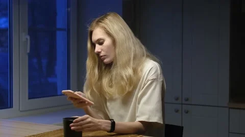Woman looking at smartphone while sitting in the kitchen at night Stock Footage 155095448