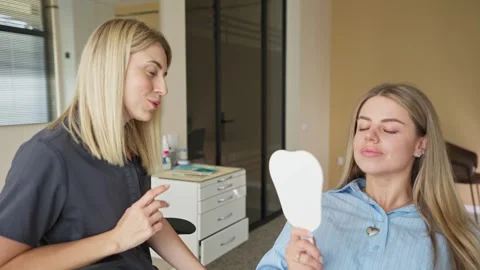 Woman looking at teeth in mirror while dentist speaks with patient in clinic. Vidéo 336199722