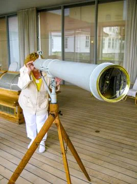A woman looks into the distance with a large white spyglass. Stock Photos
