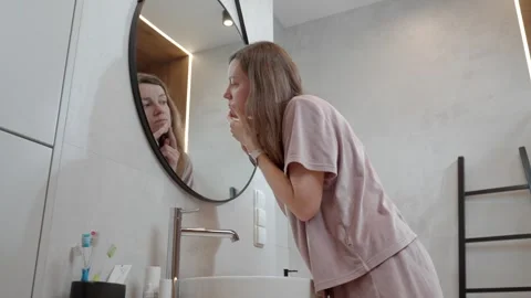 Woman looks at reflection while checking face skin near bathroom sink Stock Footage 327230825